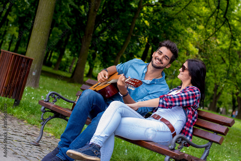 Young romantic man playing guitar for his girlfriend outdoor in summer park Young romantic man playing guitar for his girlfriend outdoor in summer park
