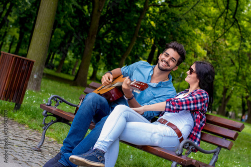 Young romantic man playing guitar for his girlfriend outdoor in summer park