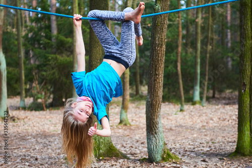 Young child girl hanging on rope upside down on playground in park