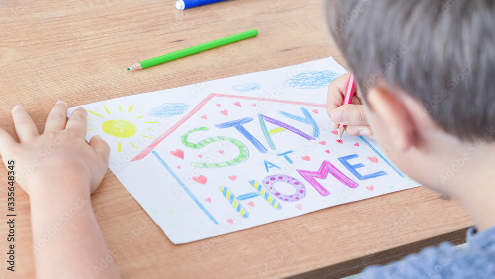 Kid drawing with colored pencils during quarantine at home. Inscription message Stay at home. Social media campaign for coronavirus prevention Kid drawing with colored pencils during quarantine at home. Inscription message Stay at home. Social media campaign for coronavirus prevention