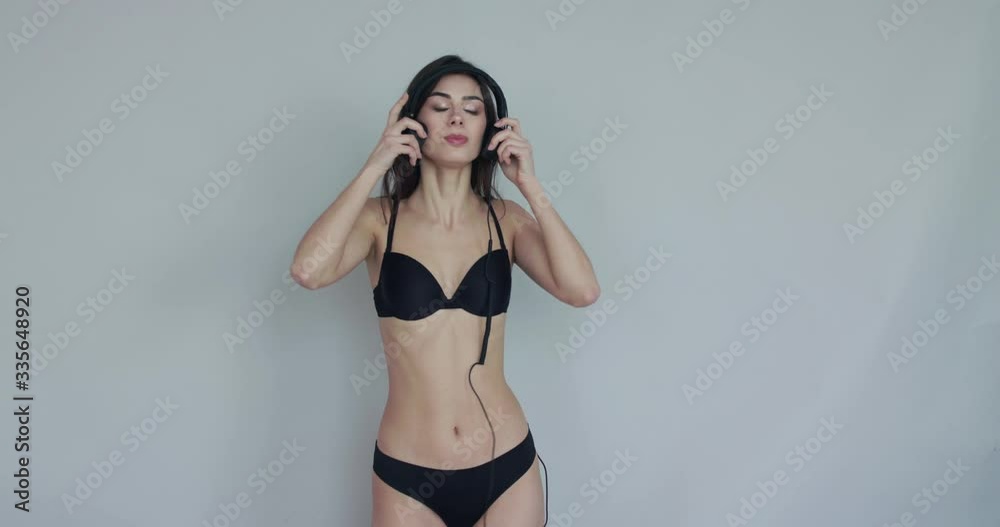 Girl in lingerie puts on headphones, nods head and dances easily on background