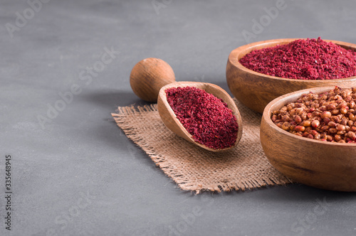 Dried ground red Sumac powder spices in wooden spoon with sumac berries on rustic table. Healthy food concept photo