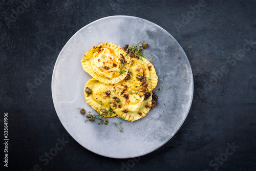 Traditional Italian ravioli pasta offered with capers and onion chili pesto as top view on a modern design plate with copy space