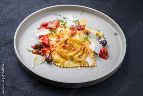 Traditional Italian ravioli pasta offered with parmesan cheese, fried tomatoes and olives as closeup on a modern design plate