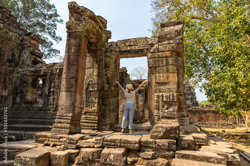 Naklejka premium Young woman with raised hands stands near entrance of ancient temple in Angkor Wat.. South Asia travel banner template. Cambodia.