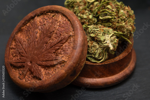 Close up of top side of wooden grinder with cannabis leaf symbol on it and green dried marijuana bud lying at the top of wooden grinder.