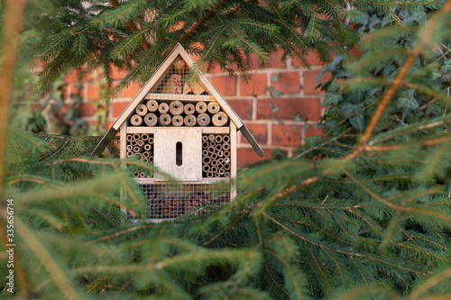 Insektenhotel aus Holz mit Röhren und Gitter vor einer Wand in einem Baum photo