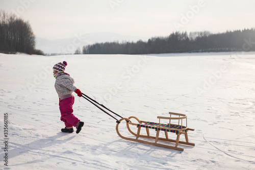 cute ittle girl haveing fun in a snow during christmas winter holiday on a sleigh. Little girl enjoy a sleigh ride. Child sledding. Toddler kid riding a sledge. Children play outdoors in snow. photo