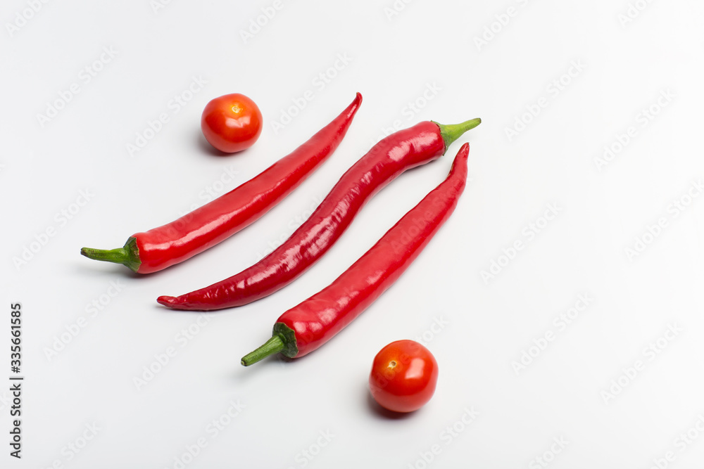 Juicy red hot chili peppers with cherry tomatoes on a branch on a white background