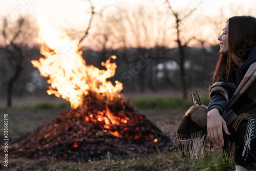 Happy young woman sitting near the evening midspring night campfire among field © Vasya