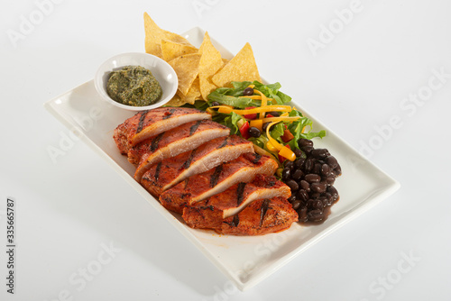 Mexican style marinated grilled chicken breast with fresh salads and green herb pesto on white rectangle plate