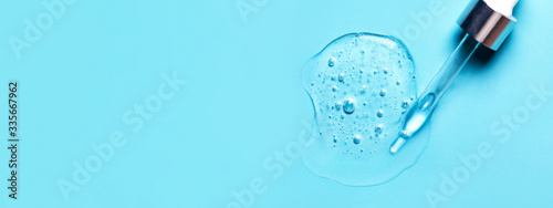 Pipette with dose of fluid hyaluronic acid on blue background. Cosmetics concept. Flat lay. Place for text.