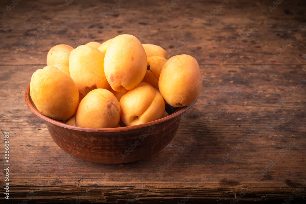 Ripe apricots berries in a clay bowl on a wooden table Ripe apricots berries in a clay bowl on a wooden table