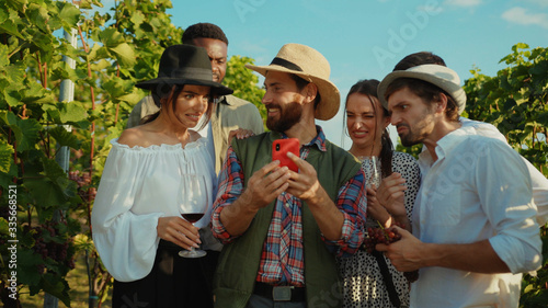 Fotografija Happy farmer showing disgusting content on smartphone and his friends screwing up faces of dissatisfaction