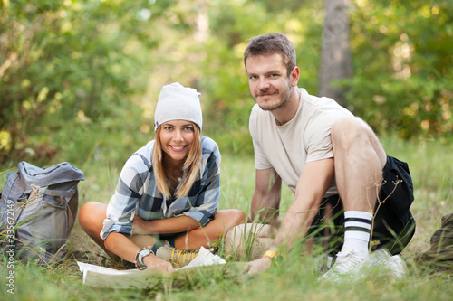 Young hikers sitting on the ground looking at an old map with a compass. Hiking couple in nature.
