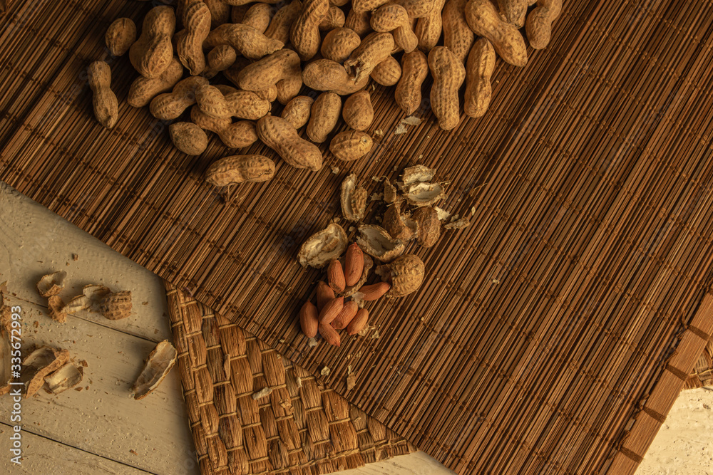 a scattering of peeled and unshelled peanuts on mats and a white wooden table
a scattering of peeled and unshelled peanuts on mats and a white wooden table