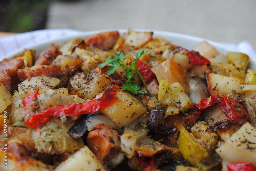 Roasted Vegetables and Sausages casserole sprinkled with seasonings, in a white ceramic bowl, close up view. Roasted Vegetables and Sausages casserole sprinkled with seasonings, in a white ceramic bowl, close up view.