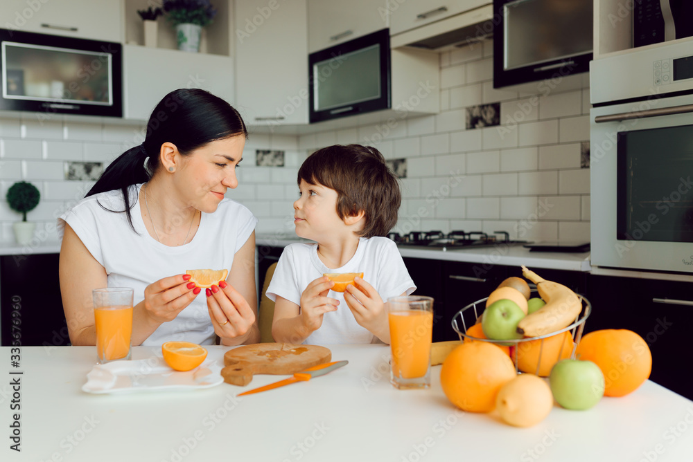 Mother and son sit in the kitchen and eat their hands. Fruit benefits concept. Healthy Eating.