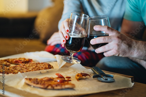A couple of men and women eat pizza on the sofa in their living room at night while watching a movie on television. Concept of life as a couple at home.