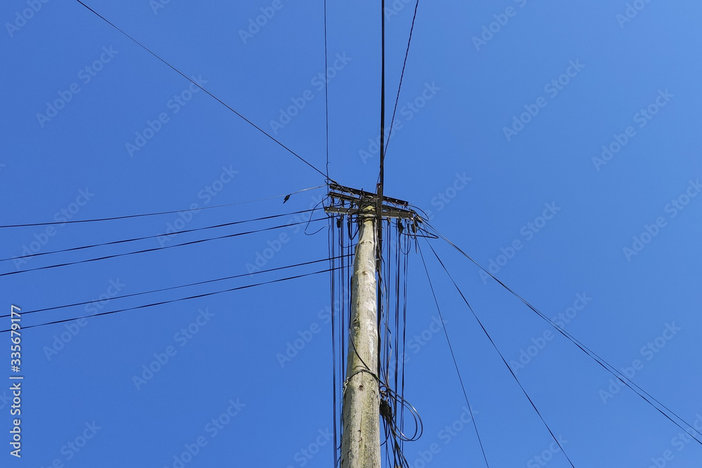 Wooden utility pole made from a single tree trunk, with many power cables and telephone cables against a deep blue sky Wooden utility pole made from a single tree trunk, with many power cables and telephone cables against a deep blue sky