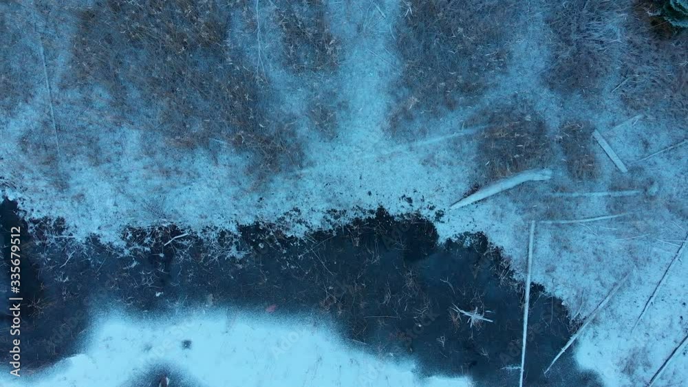 Mixture of Autumn and Winter - Drone overhead aerial view spiral above frozen shore of a lake with colorful trees