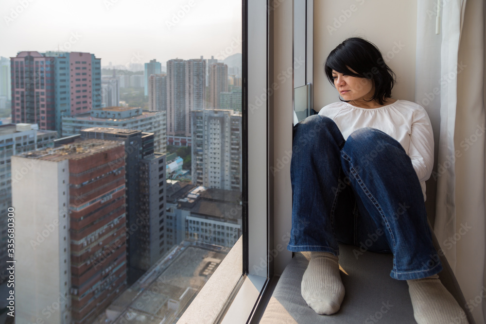 Asian girl in a skyscraper sitting at the window looking outside into the big city.