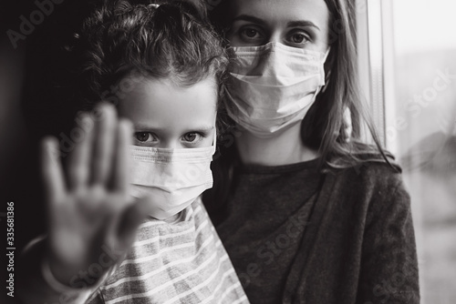 Fototapeta Naklejka Na Ścianę i Meble -  Black and white photo of mother and upset little daughter with virus mask show stop hand gesture for stop coronavirus outbreak. Self isolation, Home quarantine, prevention epidemic. Selective focus
