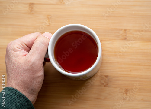 male hand holding cup of coffee on wooden background	
