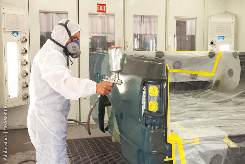 Man in Autobody Shop Painting Car Dressed in White Coveralls with Respirator On Man in Autobody Shop Painting Car Dressed in White Coveralls with Respirator On