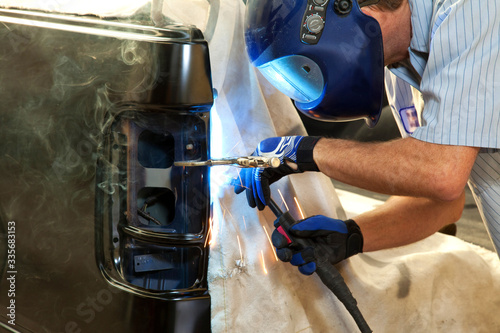 Man Welding Rear of Truck at Auto Body Repair Shop with Blue Welding Helmet and Smoke