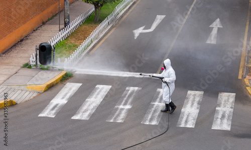 Sanitation and disinfection measures in the age of Coronavirus: A person wearing protecttive suit and respirator with filter disinfects the street