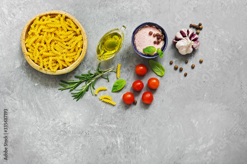 Ingredients for cooking pasta with tomato sauce. Fusilli, tomatoes, basil, olive oil, pink salt, pepper, rosemary and garlic on a gray concrete background. Top view, flat lay,copy space
