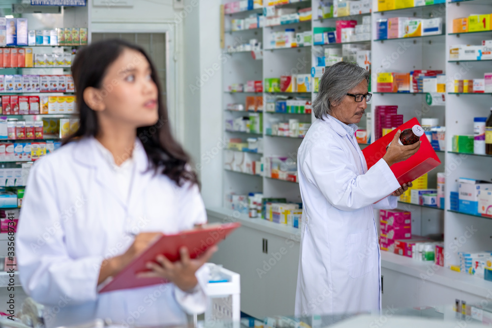 Professional Asian male and female Pharmacist checking medicines and health care product inventory stock on shelf at hospital pharmacy or drugstore. Medical, pharmaceutical and healthcare concept.