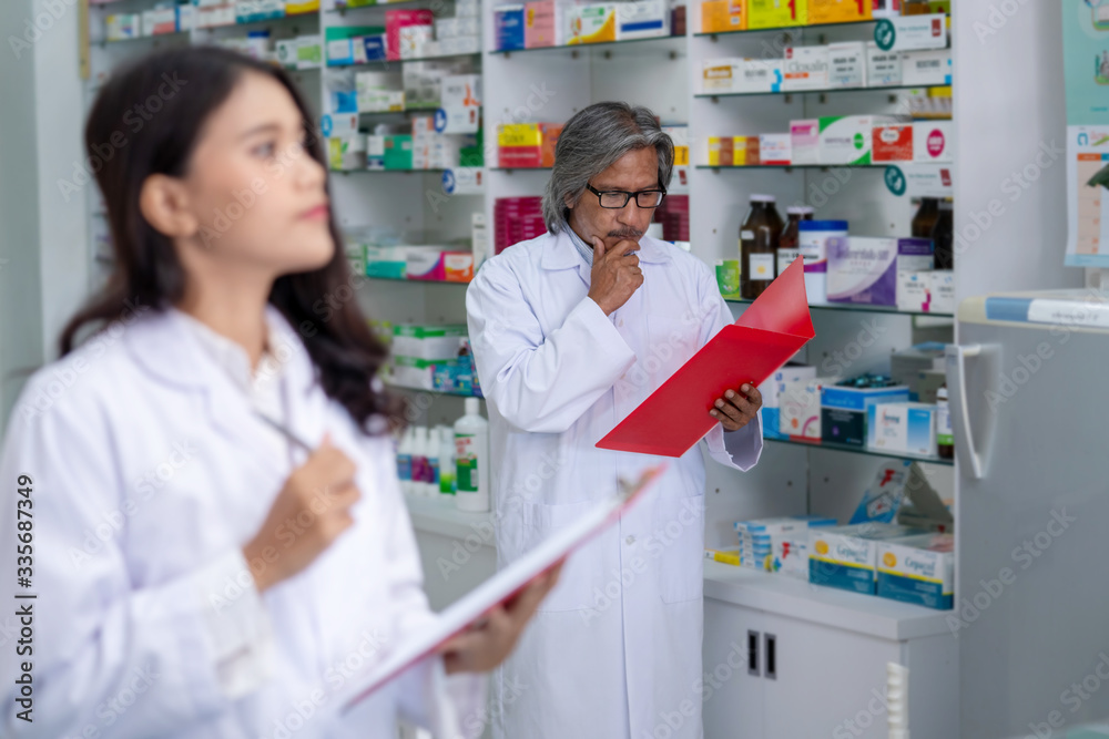 Professional Asian male and female Pharmacist checking medicines and health care product inventory stock on shelf at hospital pharmacy or drugstore. Medical, pharmaceutical and healthcare concept.