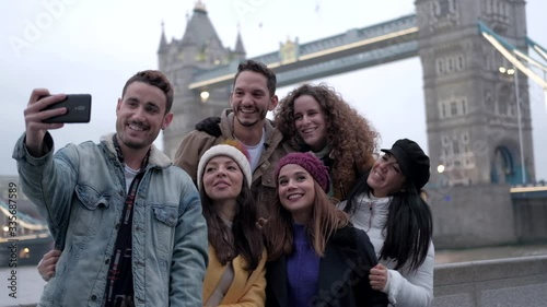A group of tourist friends take a selfie with the smartphone with the London Bridge next to the Thames