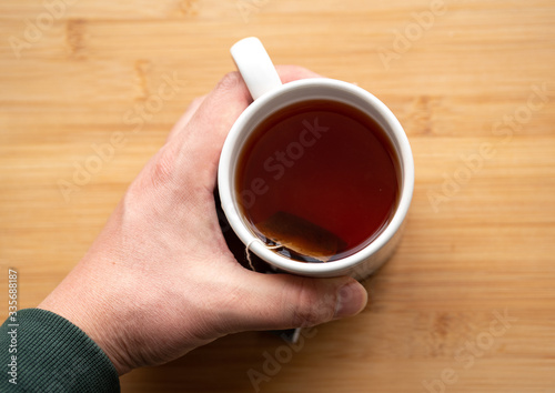male hand holding cup of coffee on wooden background 