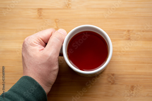 male hand holding cup of coffee on wooden background