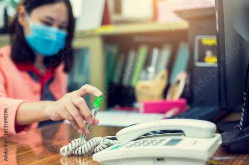 Business woman clean phone and computer keyboard with alcohol spray before touching it to preventive measures against coronavirus Covid-19 in office.