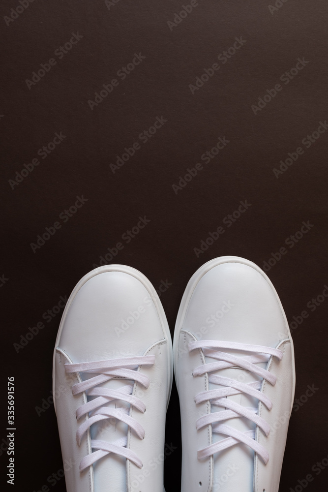 A pair of light sneakers on dark brown background. Top view. Copy space.