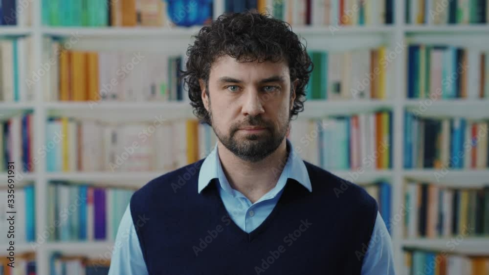 Portrait of attractive bearded curly haired man look confident and strong at camera working in the library. Real people. Caucasian ethnicity. Portrait of attractive bearded curly haired man look confident and strong at camera working in the library. Real people. Caucasian ethnicity.