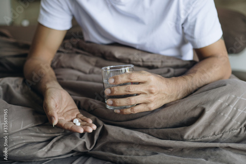 Young man sick taking medicine on the bed, Yong man taking pill and drinking water 