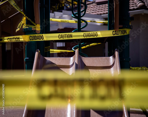 Yellow caution tape in english and spanish barring access to playgound equipment at a park. The access is denied due to the Coronavirus Pandemic photo