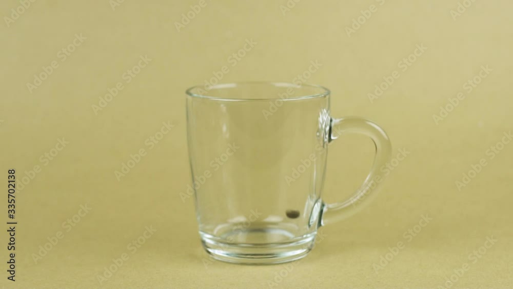 Coffee beans quickly fly, full glass cup, beige background. Energy concept