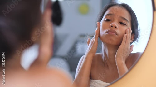 Upset young Asian woman looking face and touching skin in front of the mirror.