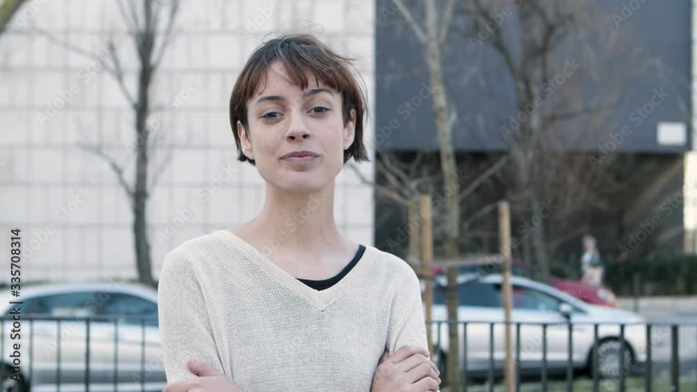 Cheerful young lady with crossed arms standing on street. Beautiful smiling young woman looking at camera. Female beauty concept Cheerful young lady with crossed arms standing on street. Beautiful smiling young woman looking at camera. Female beauty concept