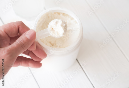 hand holding scoop of fish collagen. collagen peptides in container or jar. Copy space for text. Healthcare supplement concept. close up view on wooden background. photo