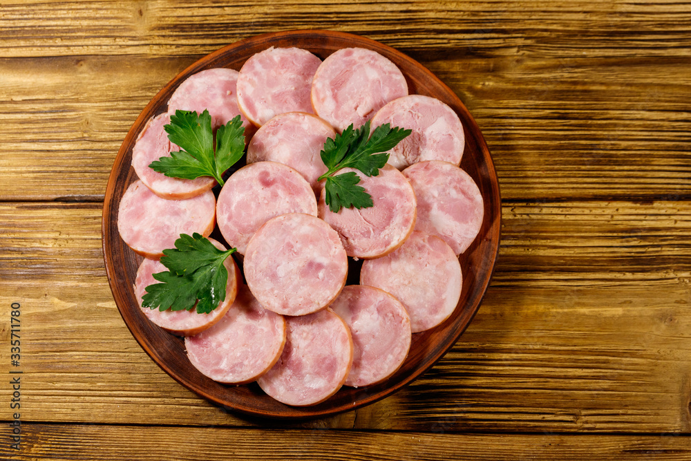 Ham sausage on a plate on wooden table. Top view