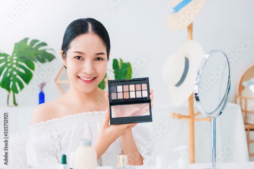 Beautiful asian woman blogger is showing how to make up and use cosmetics. In front of the camera and recording vlog video live streaming at home.Skincare for healthy face concept.