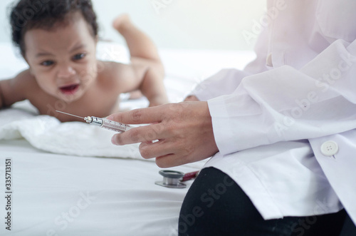 Doctor holds an injection syringe for baby , Dark skinned baby looking at doctors and crying, selective focus