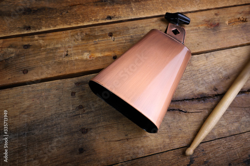 Copper Cowbell musical instrument on a wooden background with drumstick photo